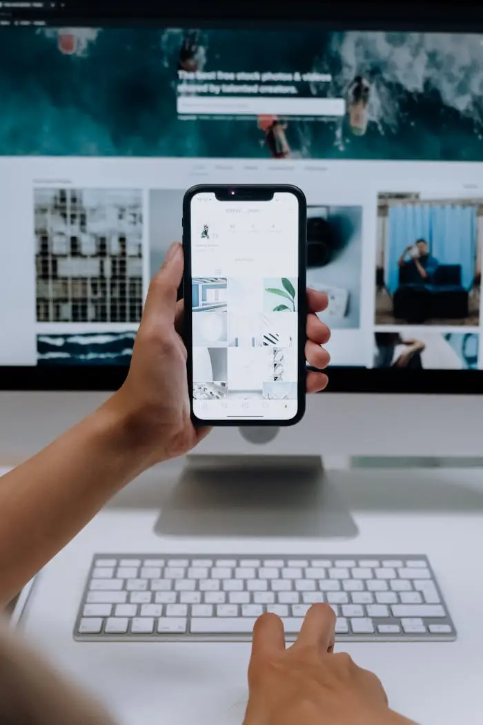 Mastering the First Impression: Your intriguing post title goes here Person uses a smartphone in front of a computer screen displaying stock photos, showcasing modern technology use.